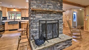 Una chimenea de piedra con una reja metálica, suelo de madera y un comedor con una silla y una mesa.