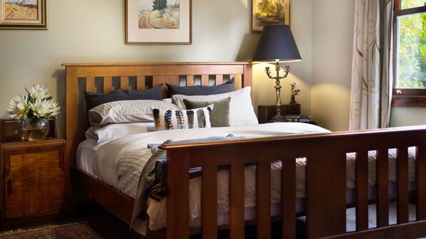 A neatly made bed with a wooden headboard, a bedside lamp, and a nightstand with a vase of flowers.