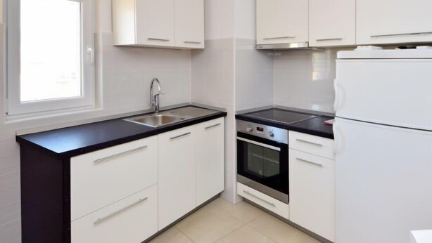 A modern kitchen with white cabinets, a black countertop, a stainless steel sink, a built-in oven, and a refrigerator. - Apartment Surjan by Interhome (Korčula/Vela Luka)
