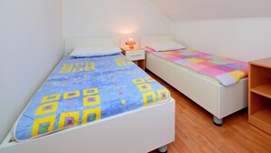 A small, well-lit room with two single beds, each with a different patterned bedspread. There is a nightstand with a lamp between the beds, and a wooden shelf to the right. - Apartment Surjan by Interhome (Korčula/Vela Luka)