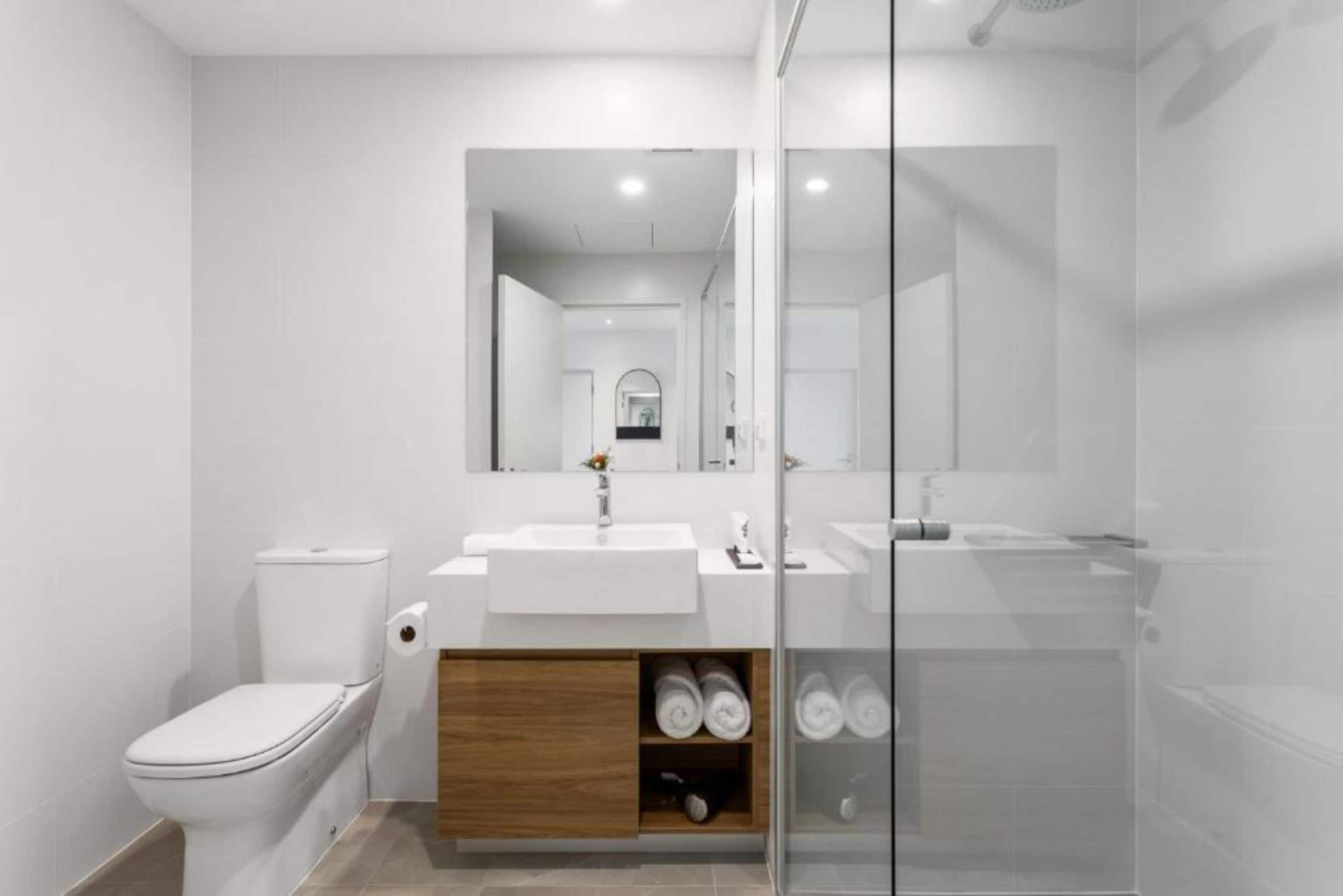 A modern bathroom with a toilet, a sink, a mirror, and a shower area.
