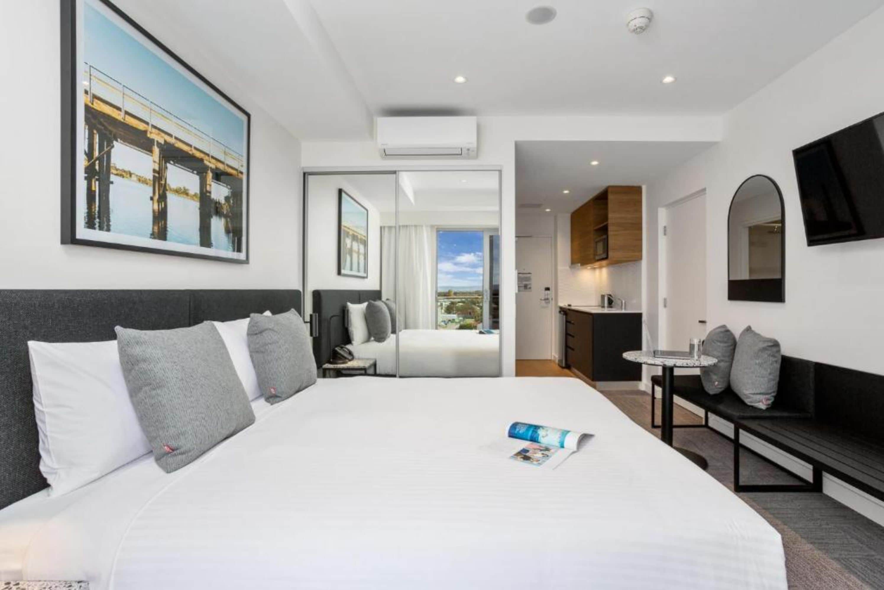 Habitación de hotel moderna con una cama grande, una kitchenette pequeña, una zona de comedor y vistas a un puente.