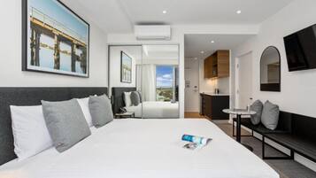 Habitación de hotel moderna con una cama grande, una kitchenette pequeña, una zona de comedor y vistas a un puente.
