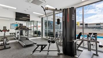 Un gimnasio con equipamiento de ejercicio, cinta de correr y vista a una piscina.