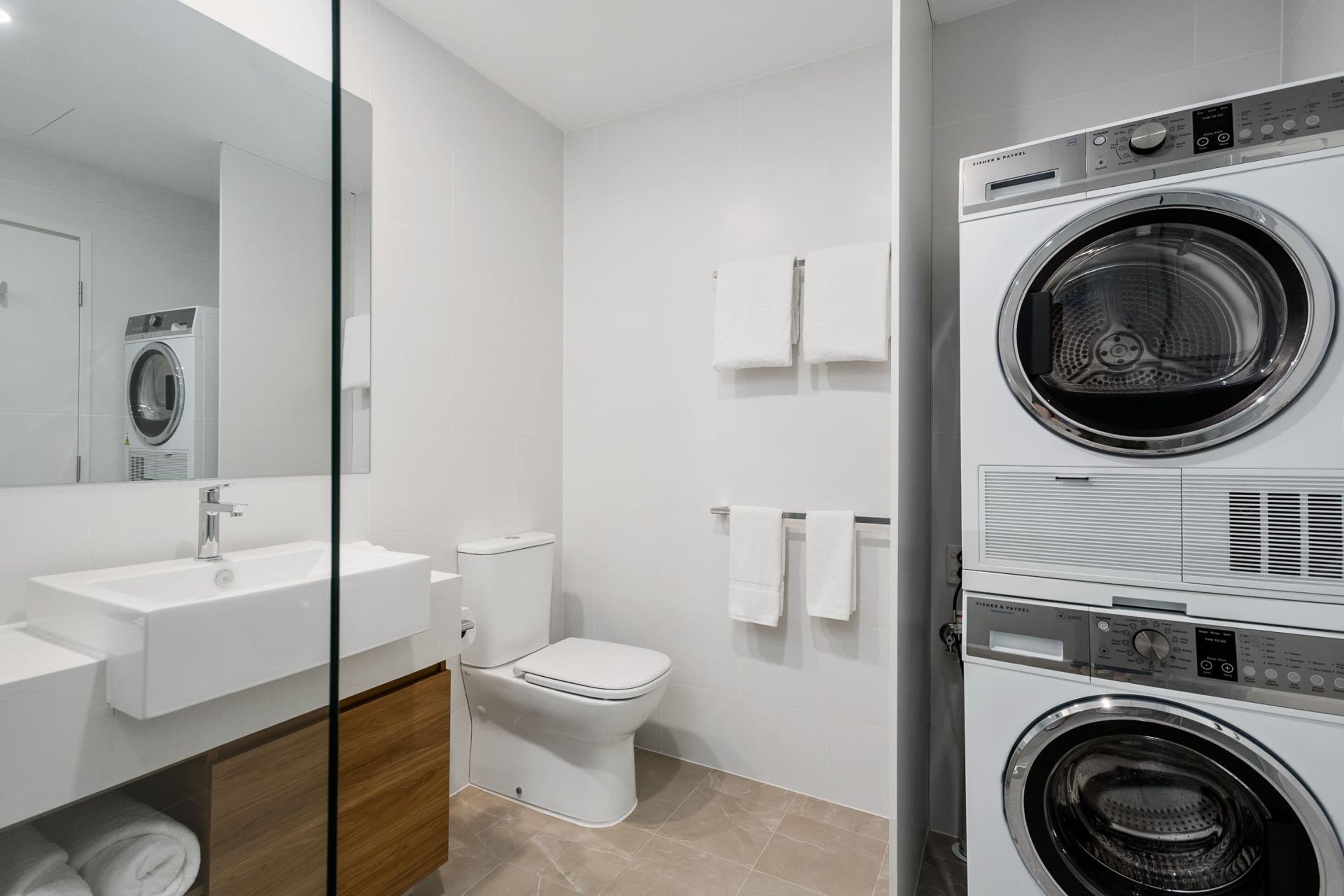 Ein modernes Badezimmer mit Waschbecken, Toilette und gestapelten Waschmaschinen.