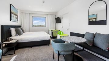Una habitación de hotel moderna con una cama, un sofá, una mesita, una silla, un escritorio, un televisor y una ventana con vistas a un puente.