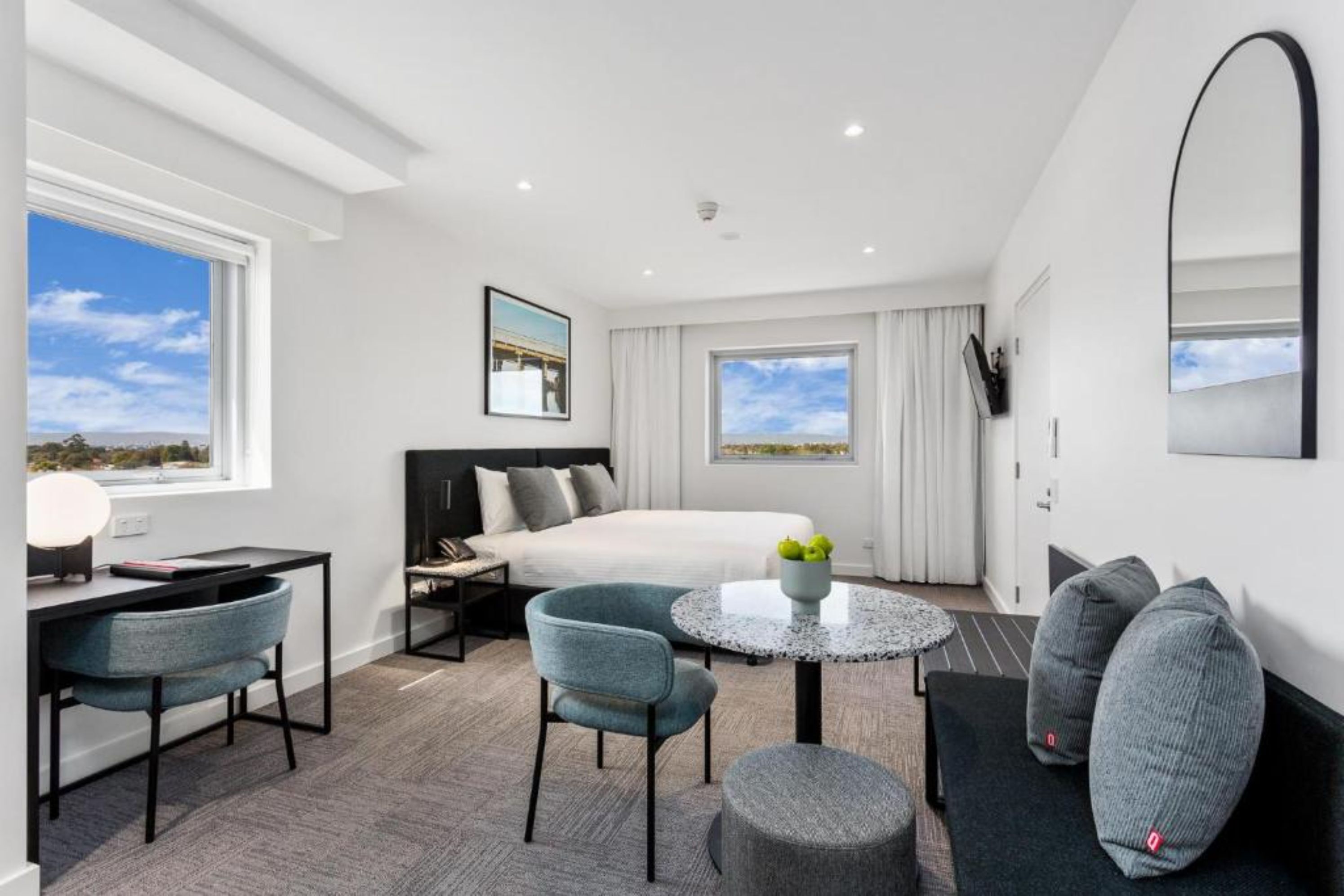 Una habitación de hotel moderna con cama, escritorio, silla, mesa redonda y un espejo grande.