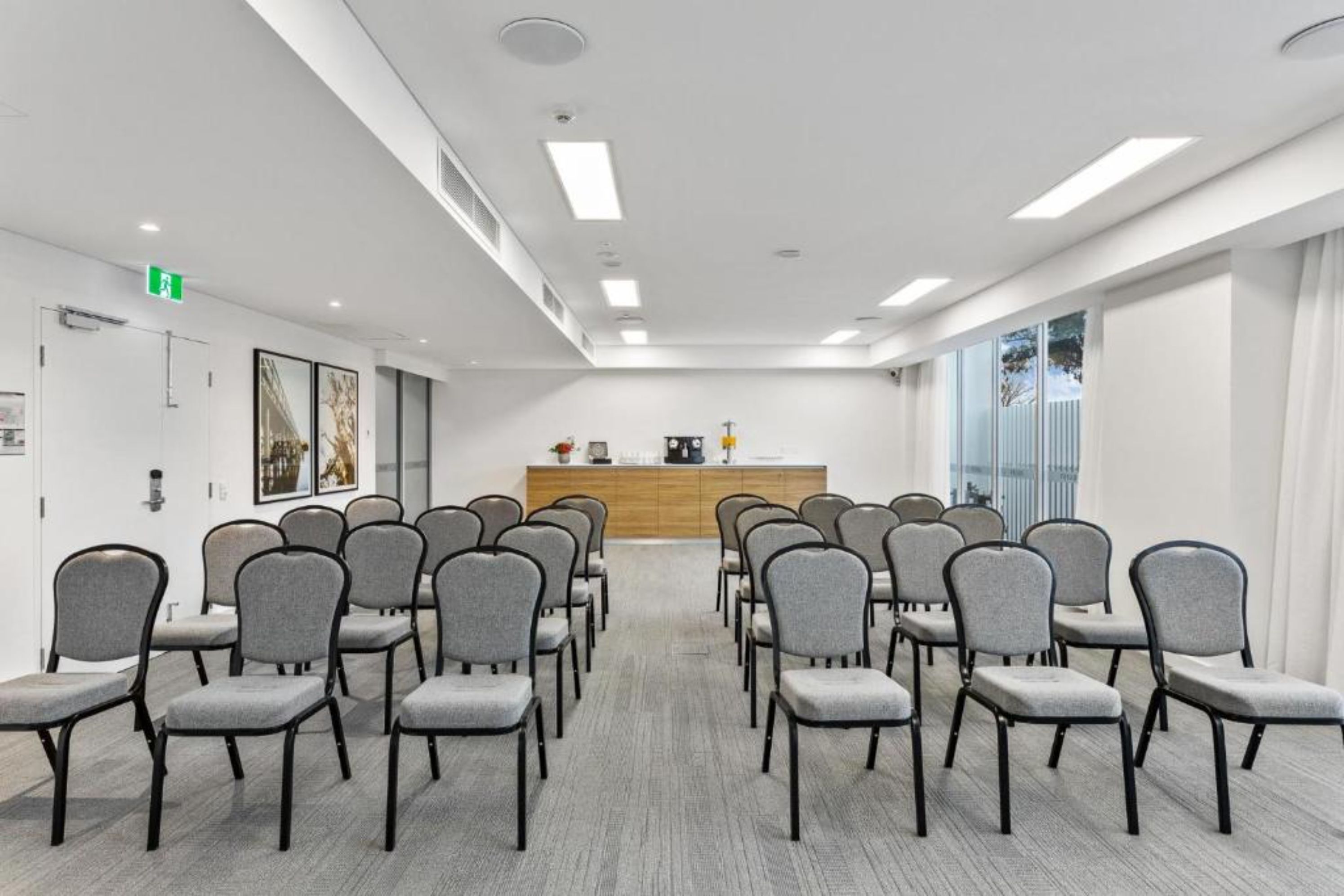 A conference room with rows of grey chairs, a wooden reception desk, and large windows with curtains.