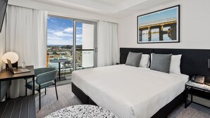 Una habitación de hotel moderna con una cama grande, un escritorio con una computadora portátil, una silla, una mesa redonda y un balcón con vista a la ciudad.