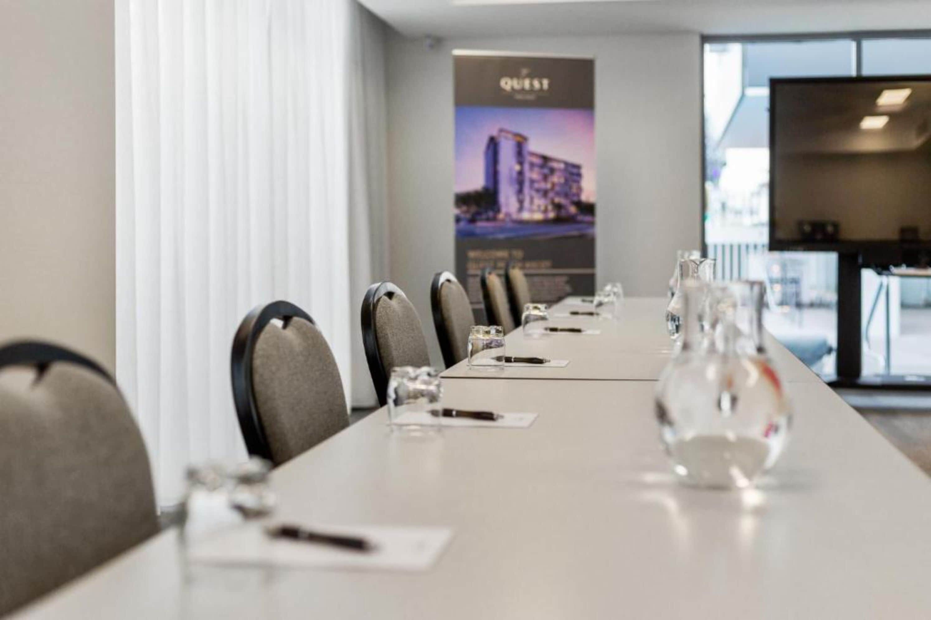 A conference room with a long table, chairs, and a poster in the background.