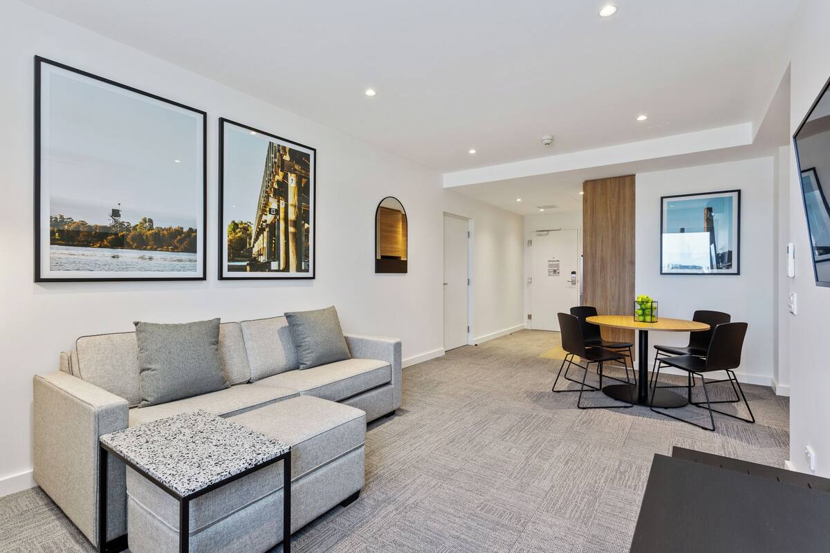 A modern living room with a sofa, coffee table, and a dining area with chairs and a table.