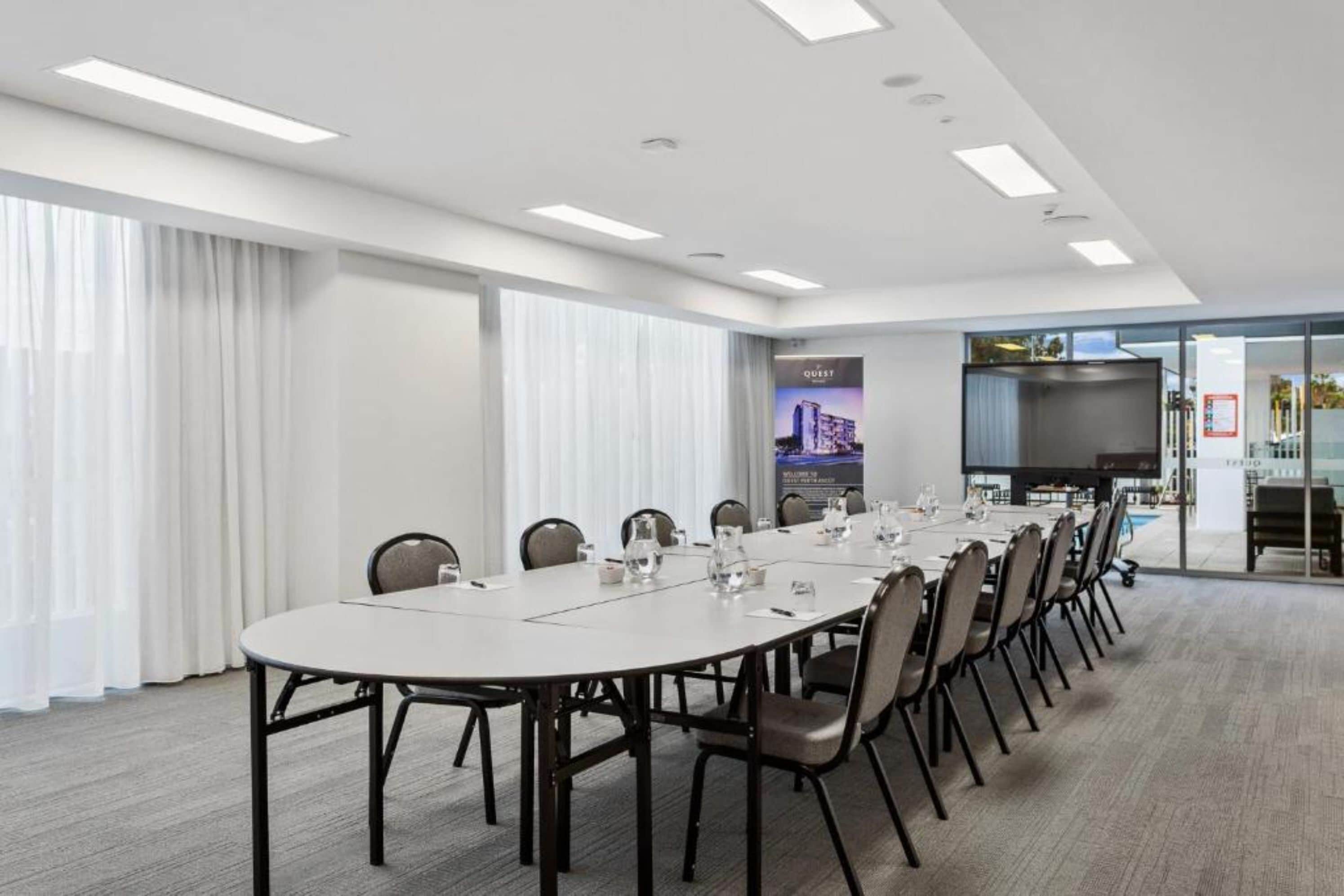 A conference room with a long table, chairs, and a large screen.