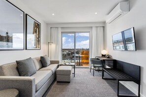 A modern living room with a sofa, a coffee table, a TV, and a balcony with a city view. - Quest Perth Ascot (Ascot)