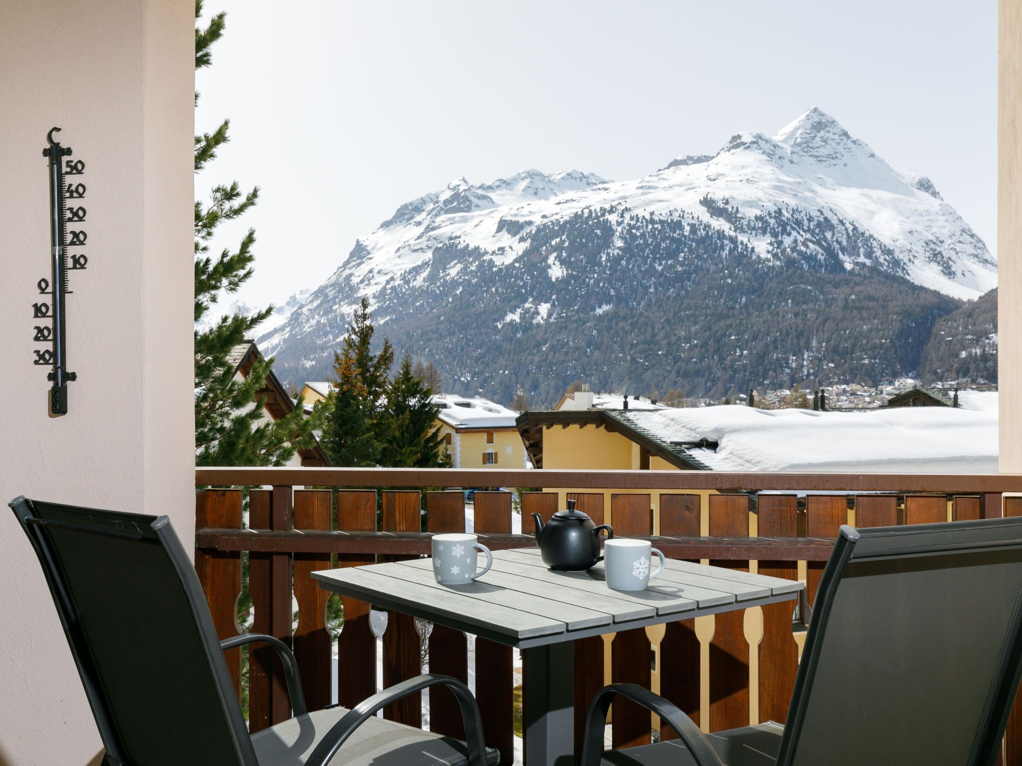 Uma varanda com mesa e cadeiras, com vista para uma montanha coberta de neve.