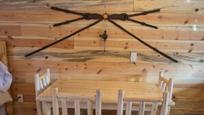 A wooden dining table with four chairs, a wall-mounted light fixture, and a wooden wall with a cross-shaped metal structure. - Tack Room Studio on 280 acre Sevier River Ranch - 1 King and 2 Twin Beds (Hatch)
