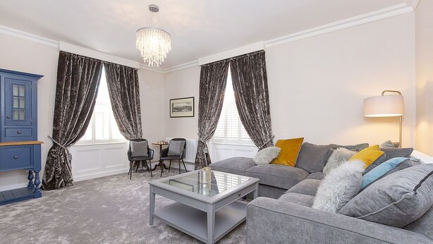 A living room with a grey sofa, a glass coffee table, a blue cabinet, and a chandelier. - George street Boutique Apartment 1 - sleeps 6 guests  in 2 bedrooms (York)