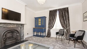 A living room with a fireplace, a blue cabinet, a television, and a window with curtains. - George street Boutique Apartment 1 - sleeps 6 guests  in 2 bedrooms (York)