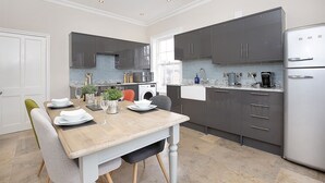Eine moderne Küche mit grauen Schränken, einem Edelstahlkühlschrank und einem Essbereich mit einem Holztisch, gedeckt für vier Personen.