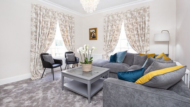 Ein Wohnzimmer mit grauem Sofa, zwei Sesseln, einem Couchtisch und einer Deckenleuchte.