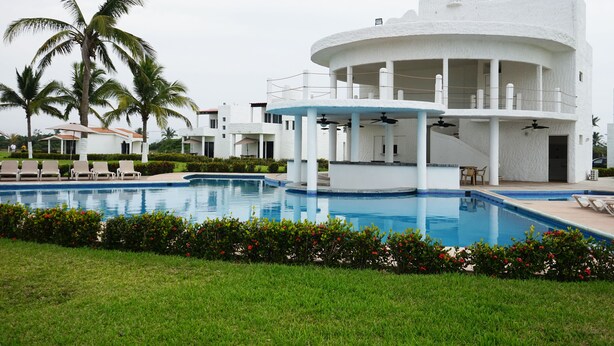 A modern building with a pool, palm trees, and a well-maintained lawn. - Color Marino Seaside Hotel (Escuinapa)
