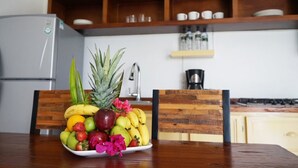 A kitchen with a wooden dining table, a fruit bowl, and a refrigerator. - Color Marino Seaside Hotel (Escuinapa)