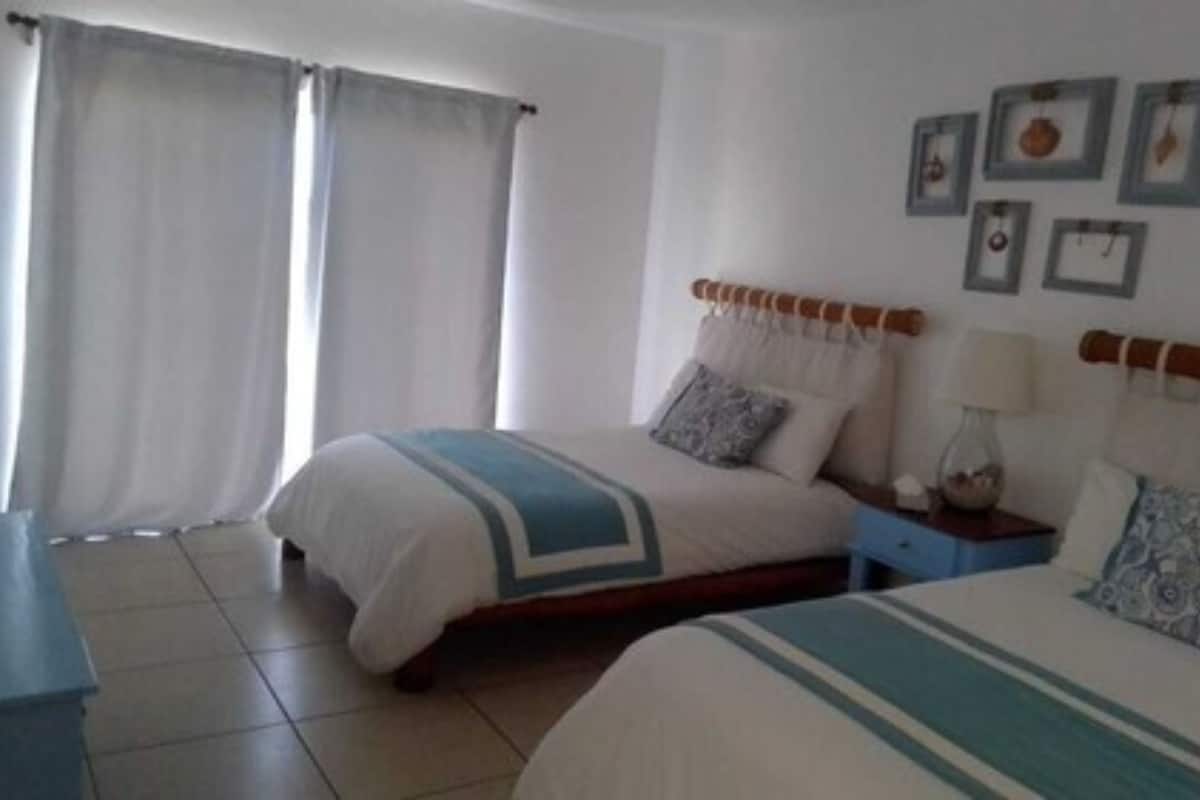 Una habitación de hotel con dos camas, una mesita de noche, una lámpara y una pared decorada con cuadros.