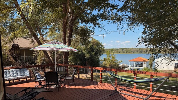 Eine Holzterrasse mit Gartenmöbeln, einer Hängematte und Blick auf einen See.