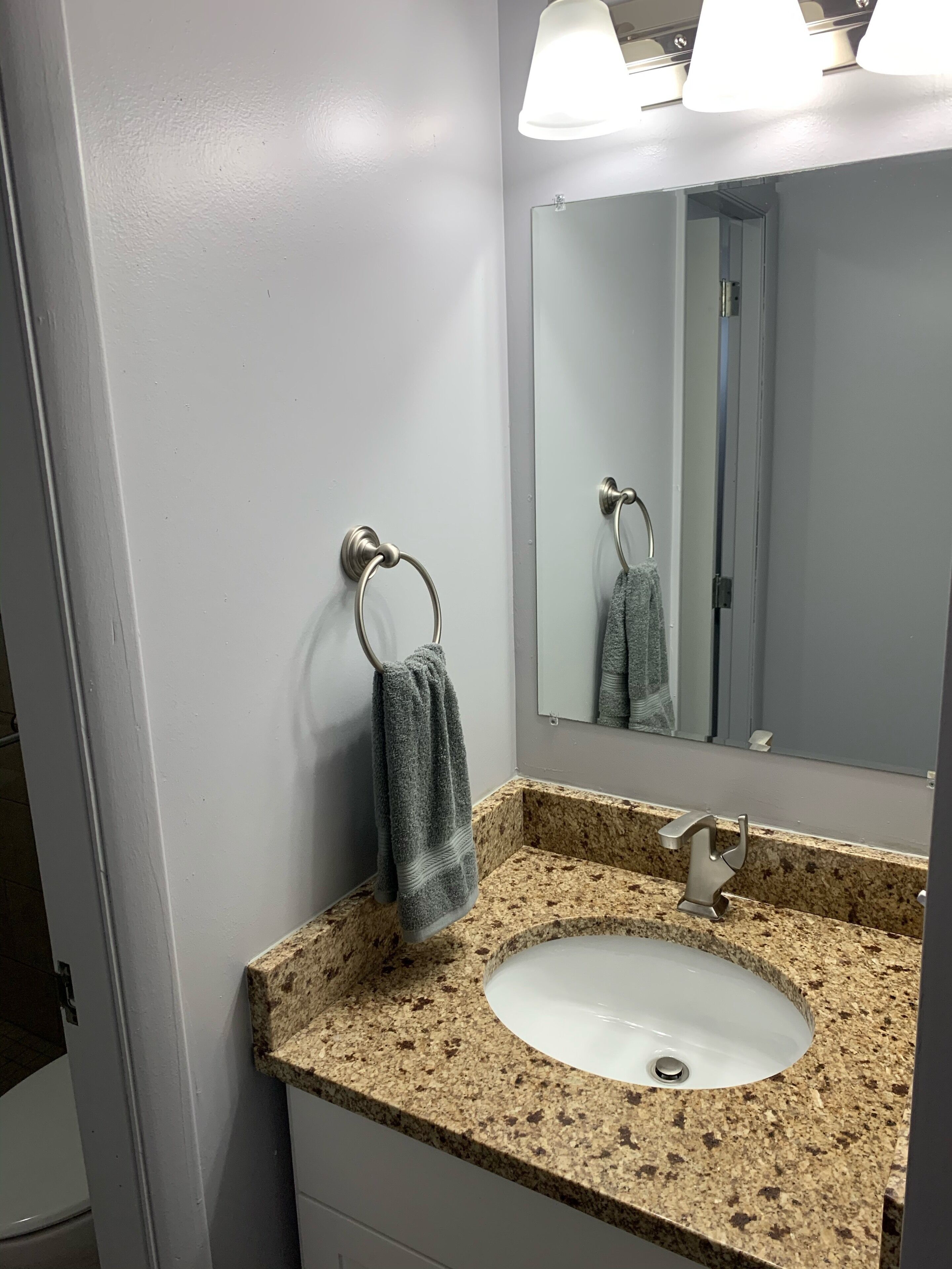 A bathroom with a granite countertop, a sink, a mirror, and a towel rack.