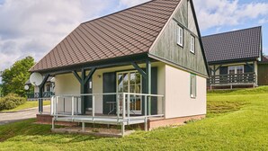 Une maison de plain-pied avec un toit en pente, une véranda dotée d’une balustrade et une petite terrasse.