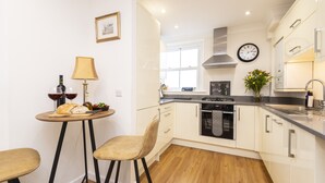Een moderne keuken met witte kasten, een houten aanrecht, een ingebouwde oven en een klok aan de muur.