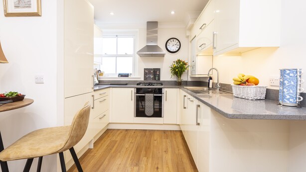 Een moderne keuken met witte kastjes, een roestvrijstalen afzuigkap, een ingebouwde oven, een spoelbak en een klok aan de muur.