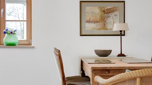 A dining area with a table, chairs, a vase with flowers, a painting on the wall, and a lamp. - Charming Apartment “Holunder” with Mountain View, Wi-Fi, Balcony & Garden (Bad Tölz)