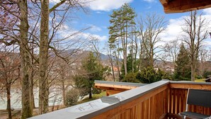 A balcony with a view of trees and mountains, a wooden deck, and a chair. - Charming Apartment “Holunder” with Mountain View, Wi-Fi, Balcony & Garden (Bad Tölz)