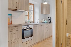 A modern kitchen with light wood cabinetry, a built-in oven, a window, and a coffee maker.