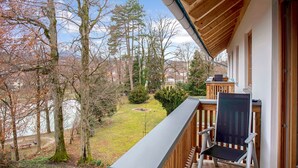 A balcony with a view of a forest and a lake, a wooden deck, and a chair. - Charming Apartment “Ferienwohnung Birke” with Mountain View, Wi-Fi (Bad Tölz)