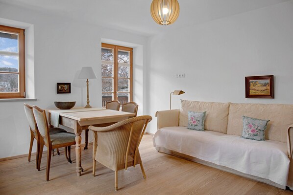 A room with a dining table, chairs, a sofa, a lamp, and a painting on the wall.
