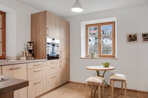 Une cuisine moderne avec des meubles en bois, un four encastré, une machine à café et une fenêtre donnant sur des maisons.