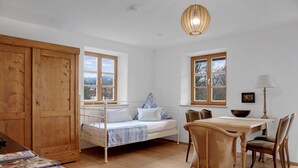 A bedroom with a bed, a dining table with chairs, a wooden wardrobe, and a window with a view. - Charming Apartment “Ferienwohnung Birke” with Mountain View, Wi-Fi (Bad Tölz)