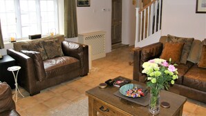 A living room with two brown leather sofas, a coffee table with a vase of flowers, and a window with curtains. - 'The Old Customs House', character cottage on Mudeford Quay (Christchurch)