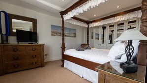 A bedroom with a four-poster bed, a wooden dresser, a flat-screen TV, and a lamp on a glass table. - 'The Old Customs House', character cottage on Mudeford Quay (Christchurch)