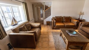 A living room with a brown leather sofa, a wooden coffee table, and a window with curtains. - 'The Old Customs House', character cottage on Mudeford Quay (Christchurch)
