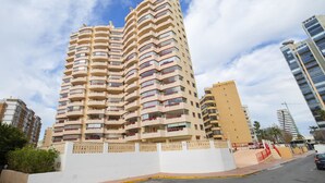 Ein hoch aufragendes Wohngebäude mit mehreren Balkonen, heller Fassade und blauem Himmel.