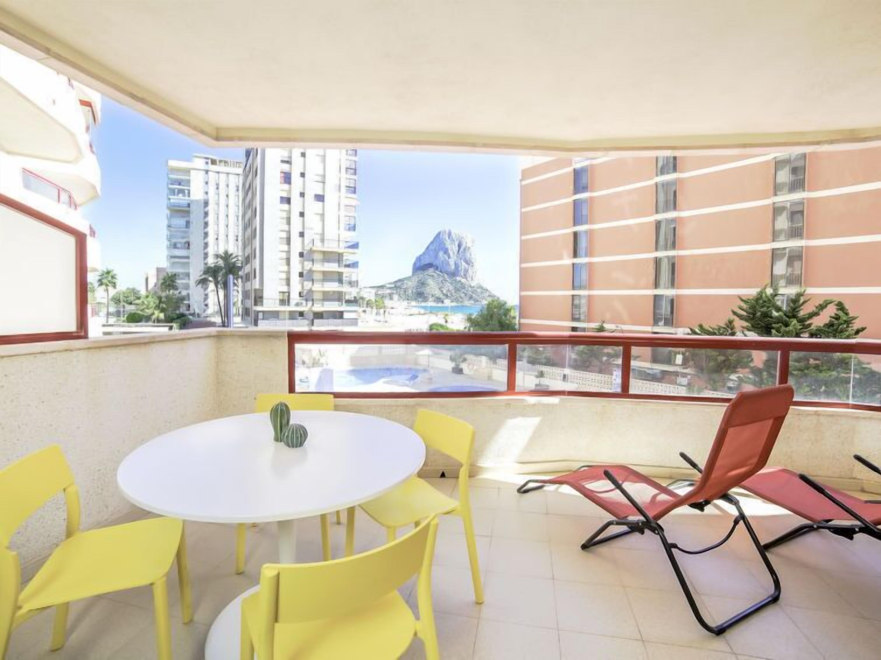 A balcony with yellow chairs, a white table, and a red chair.