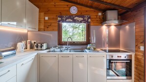 A modern kitchen with white cabinets, a built-in oven, a sink, and a window with a floral curtain.