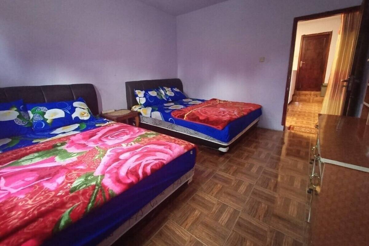 A room with two beds, each with floral bedding, a wooden floor, and a door leading to another room.