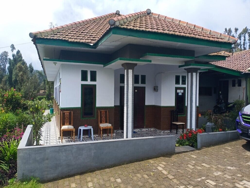 A two-story house with a tiled roof, a covered porch, and a small garden area with chairs and plants.