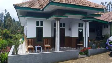 A two-story house with a tiled roof, a covered porch, and a small garden area with chairs and plants.