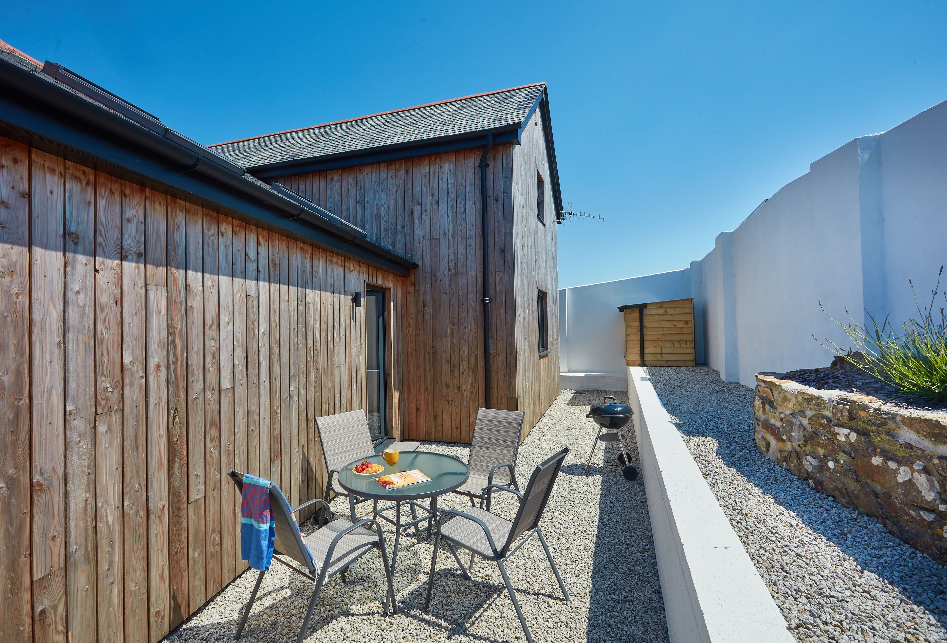 A wooden building with a sloped roof and a small patio area with a round table and chairs.