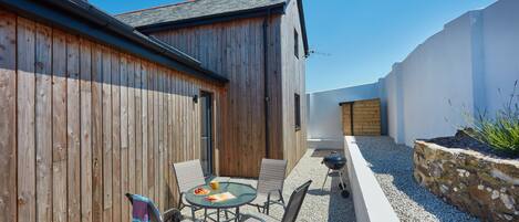 A wooden building with a sloped roof and a small patio area with a round table and chairs.
