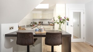 A modern kitchen with a central island, two bar stools, and a vase with flowers. - The Penthouse Fistral Beach -  an apartment overlooking Fistral Beach sleeping six (Newquay)